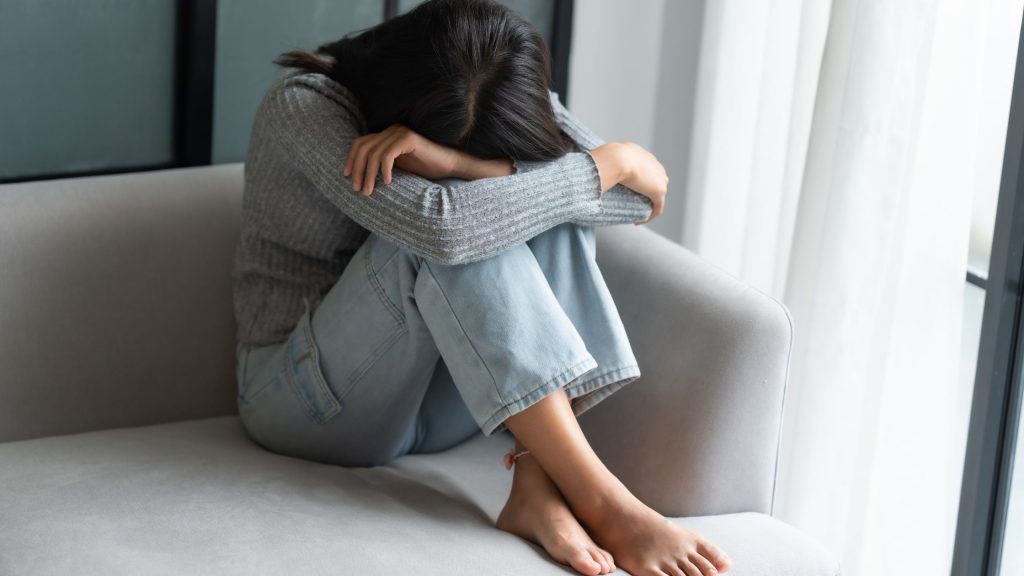 sonna stressata secudata sul divano, il capo fra le ginocchia, a piedi nudi