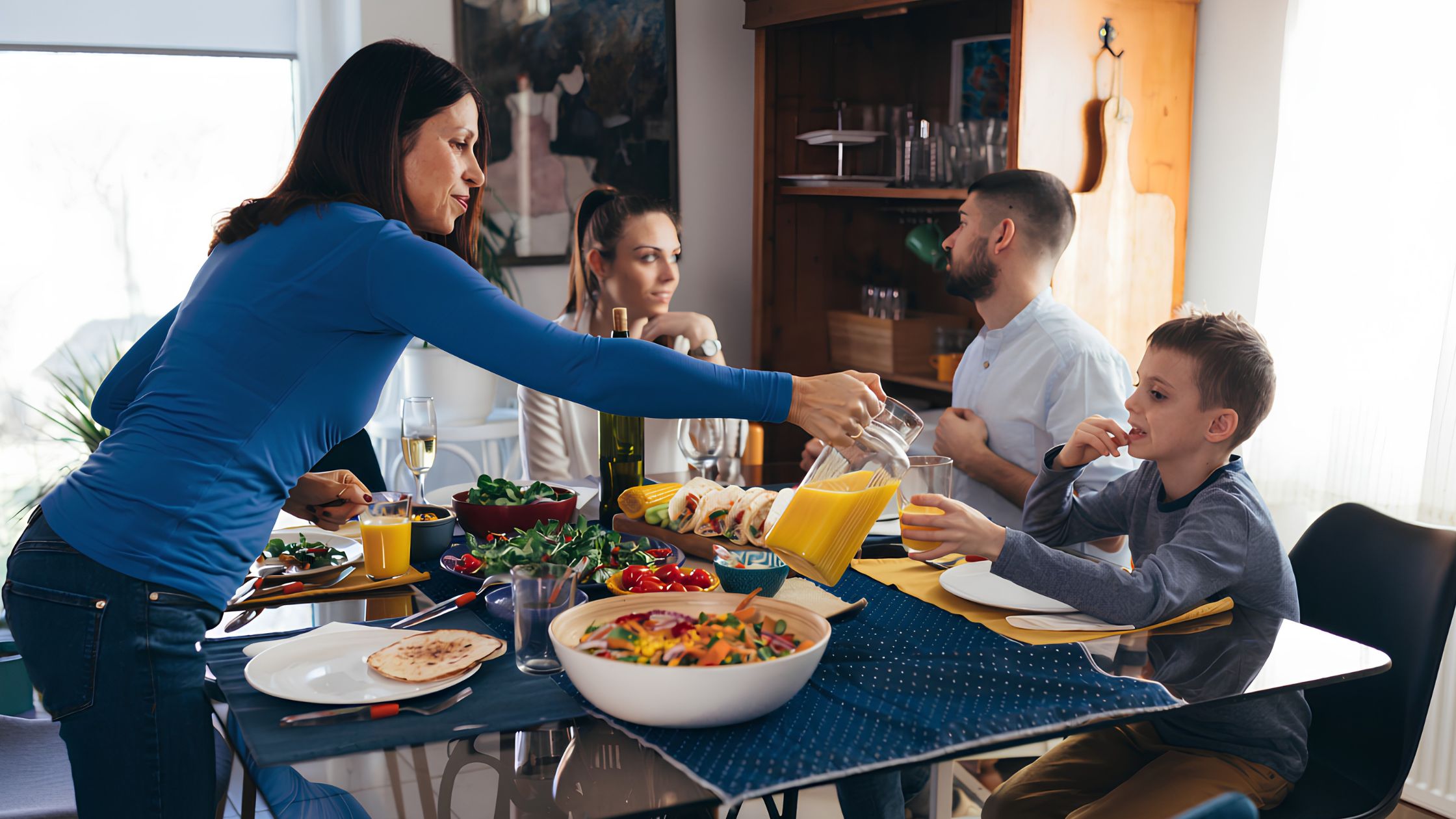 Una famiglia a tavola durante un pasto diurno con insalate fresche, verdure e spremuta d'arancia per un'alimentazione sana e bilanciata.